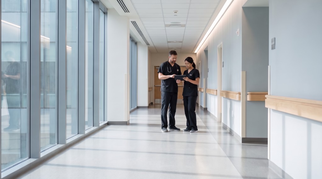 Clinical staff reviewing a tablet together in a skilled nursing facility hallway.